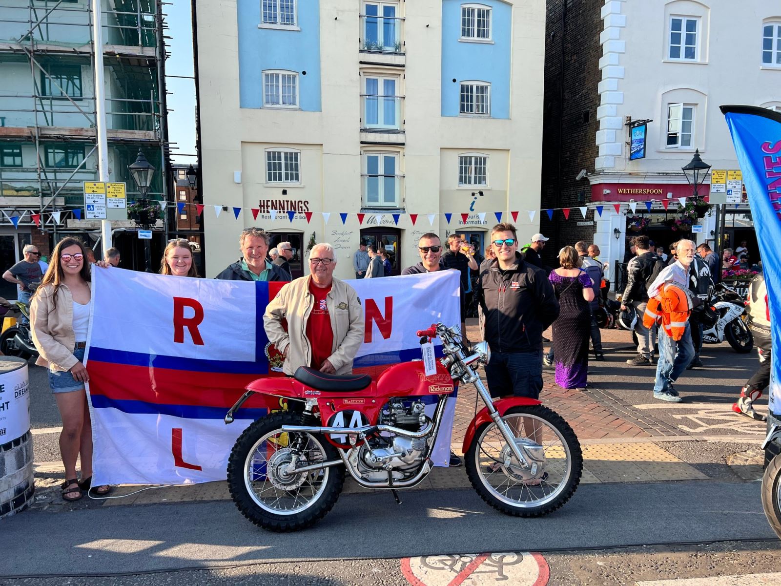 Group of people standing next to winning bike and holding a flag up 